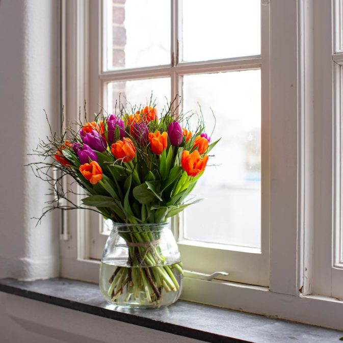 oranje met paarse tulpen in het raam vier de lente bloemen bezorgen.